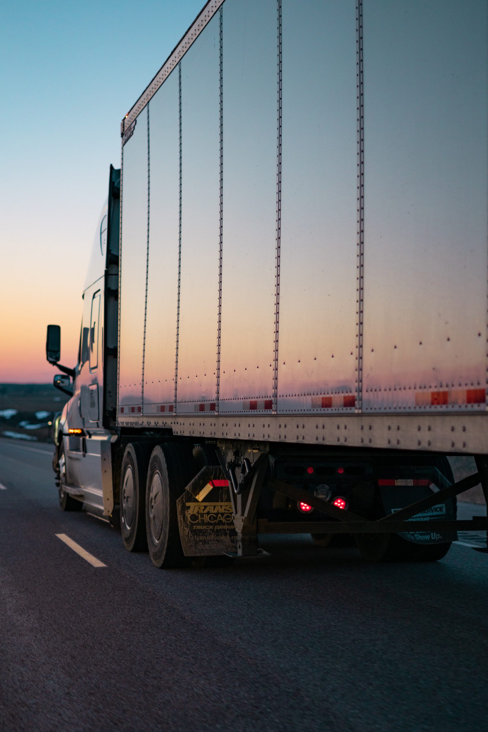Tractor-trailer driving into the sunset with dusky sky