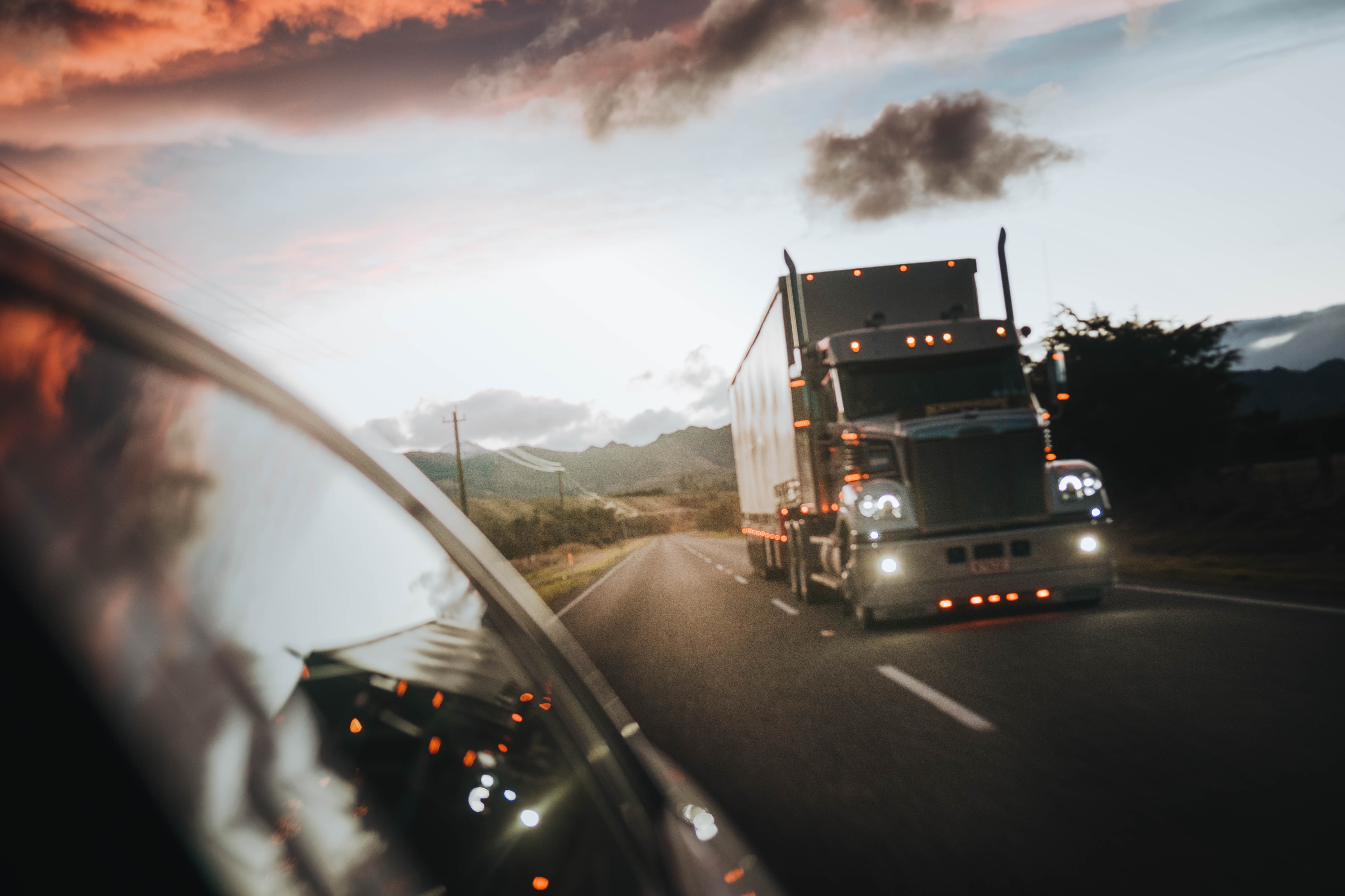 View from a passenger car showing a semi truck approaching at sunset