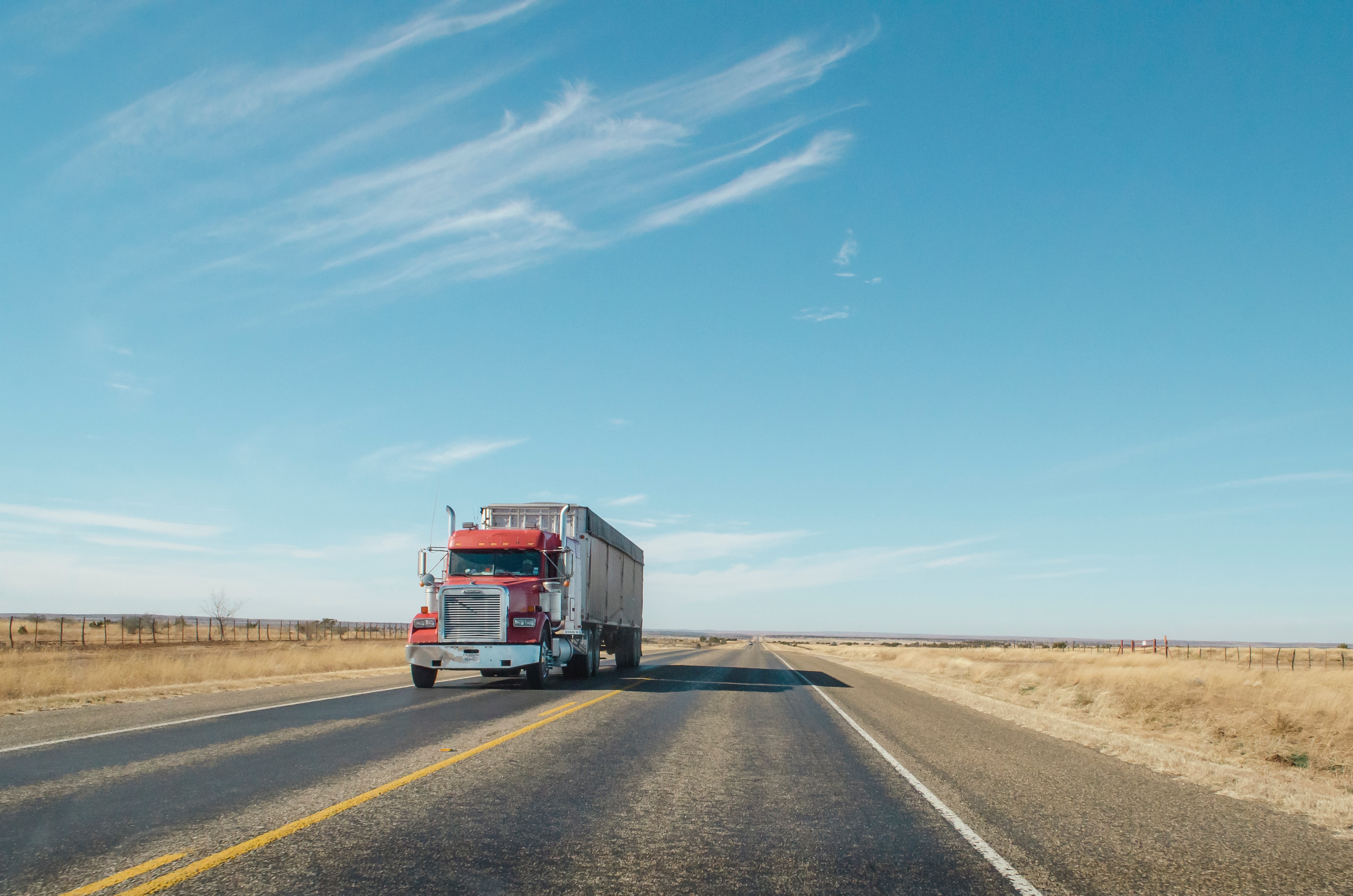 Red semi truck on an open highway under a clear sky